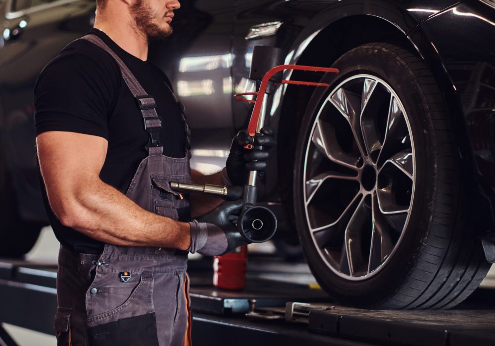 Muscular man is fixing car's wheel with special tool at auto service.